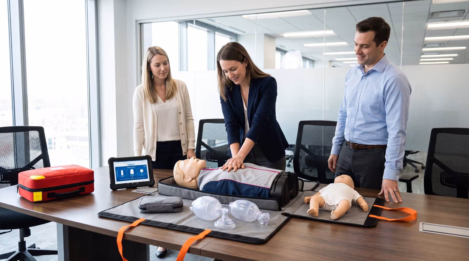 Office employees practicing CPR on adult and infant manikins with a Go-Kit on a conference table